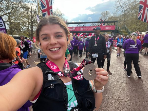 A smiling marathon runner holds her medal at the finish line