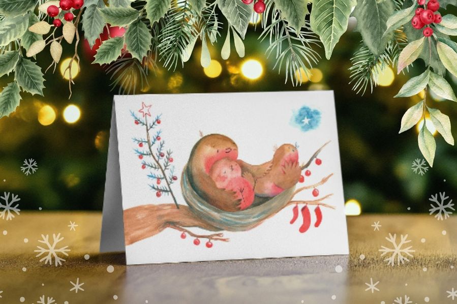 A Christmas card on a table with some Christmas decorations surrounding it.